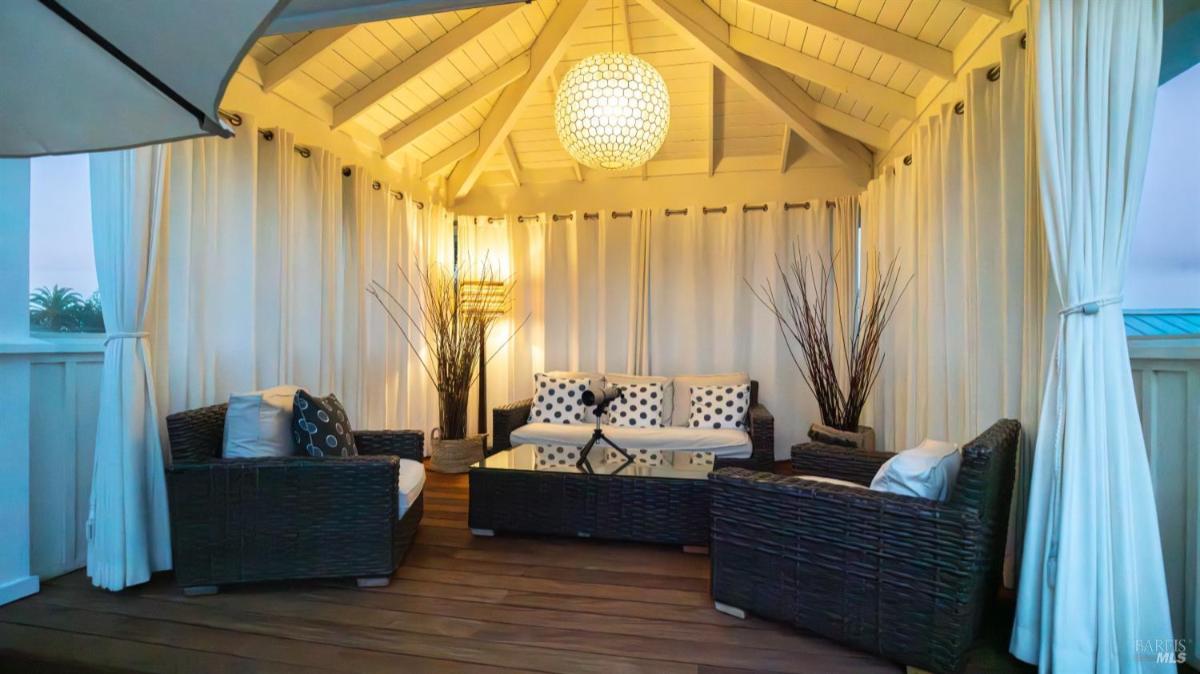 Covered seating area with wicker furniture and curtains on a rooftop deck.