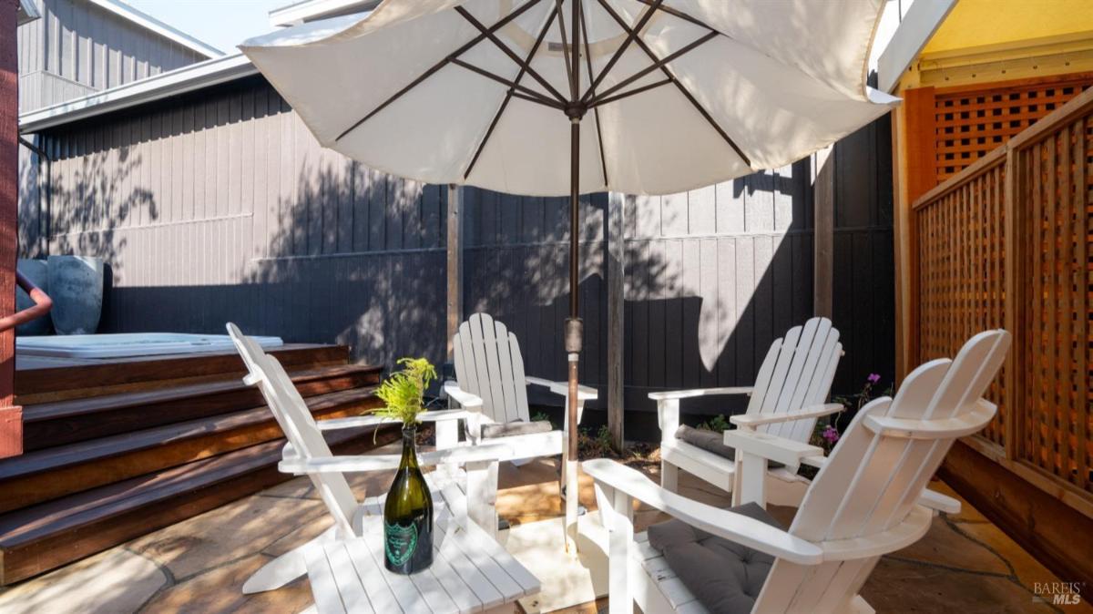 Four white wooden chairs and a table with an umbrella in an outdoor patio setting.