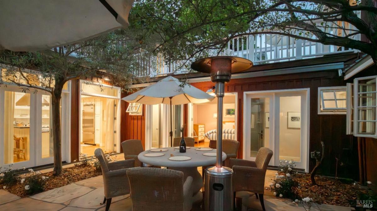 Outdoor dining area with a round table, chairs, and umbrellas near open doors leading inside.