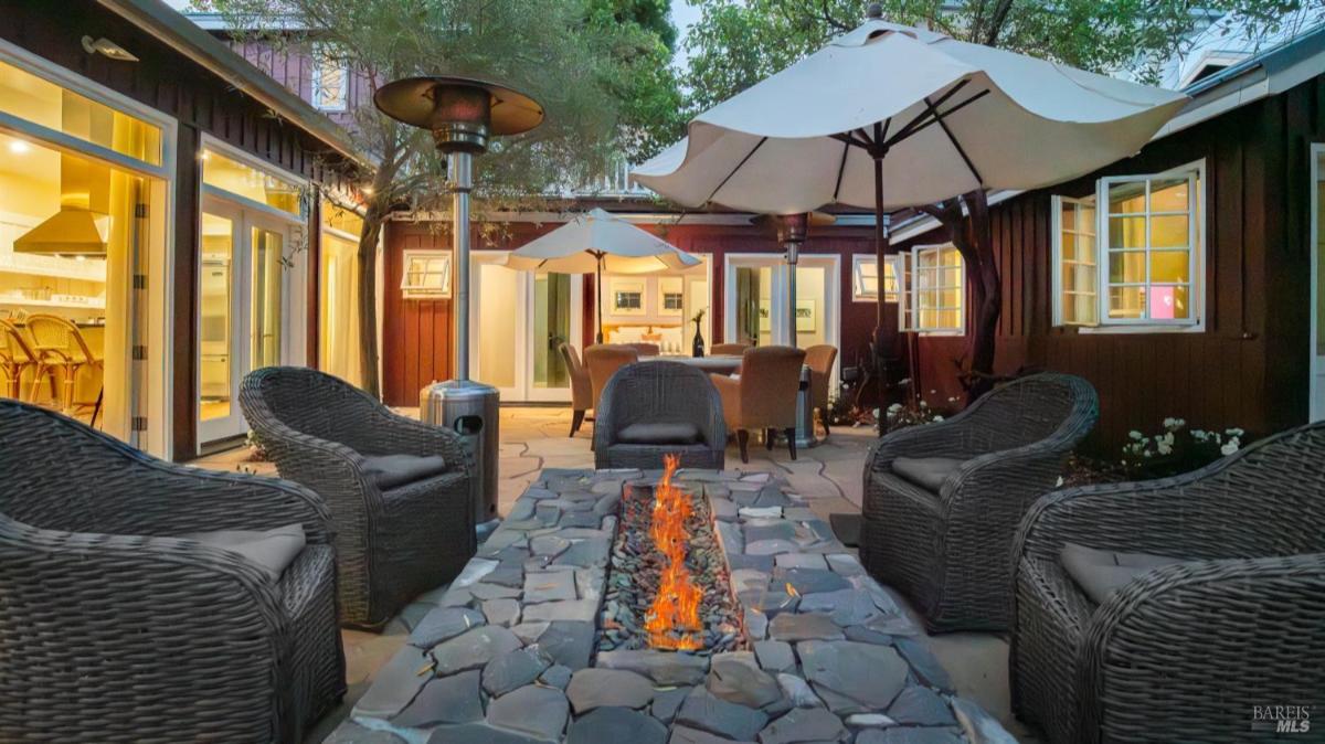 Firepit surrounded by chairs and tables with umbrellas in an outdoor courtyard.