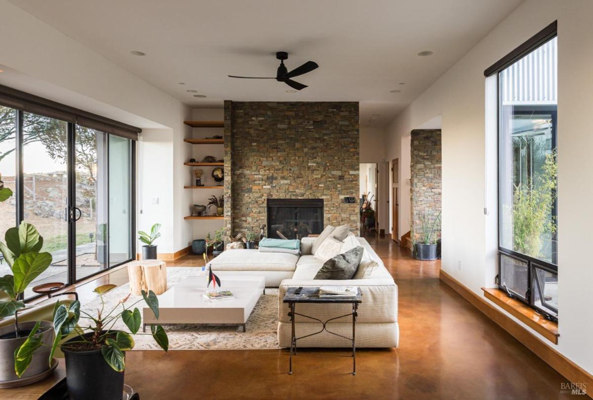 A room with a stone fireplace, white sectional sofa, and large windows.