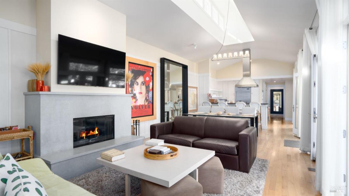 Living room with a wall-mounted TV, fireplace, and seating, leading to an open kitchen.