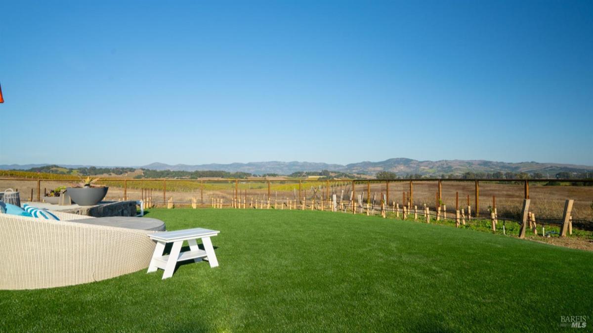 Open field with a fenced border, a fire pit, and seating facing distant hills.