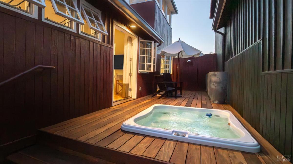 Outdoor hot tub on a wooden deck with doors leading into the house.