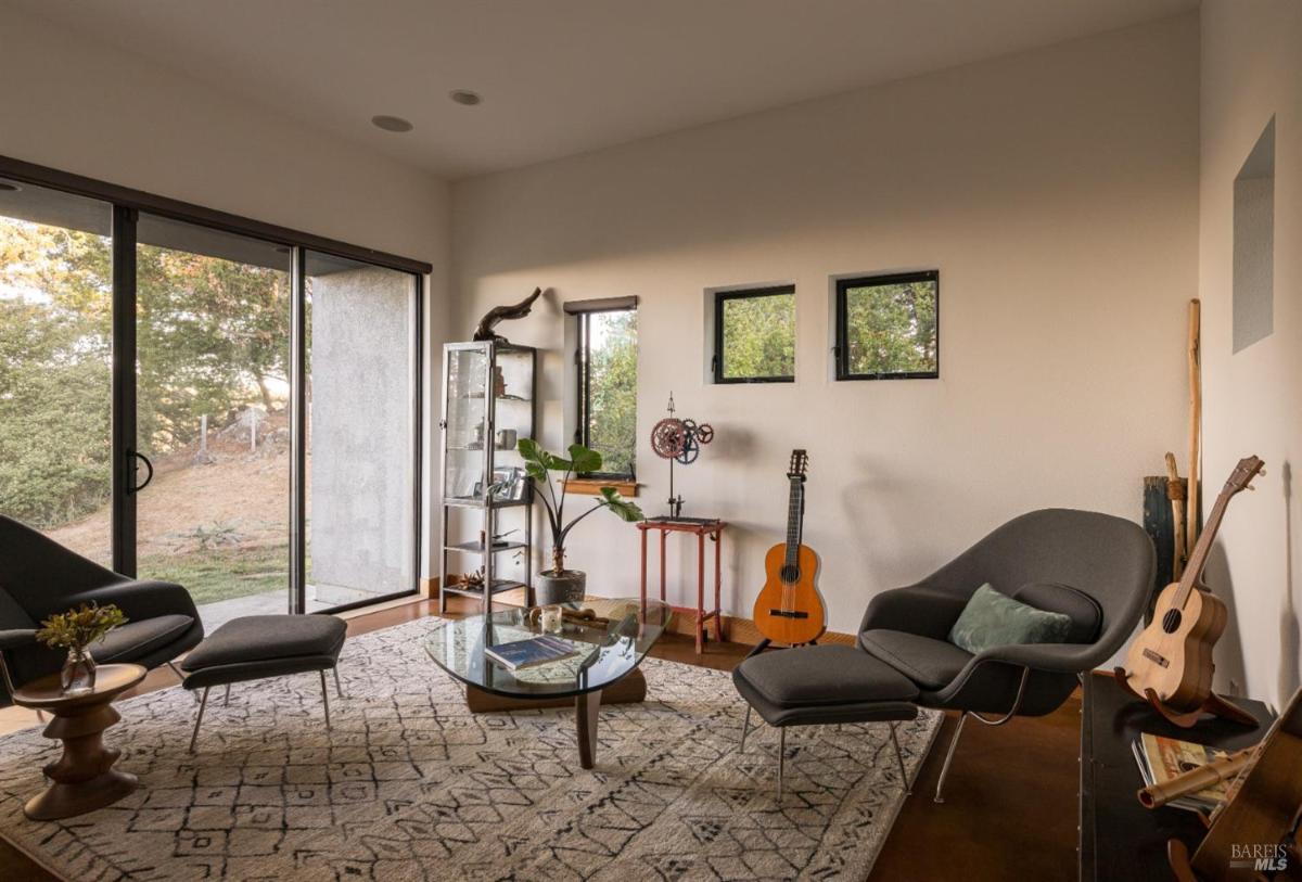 A cozy space with a guitar, modern chairs, and sliding glass doors.