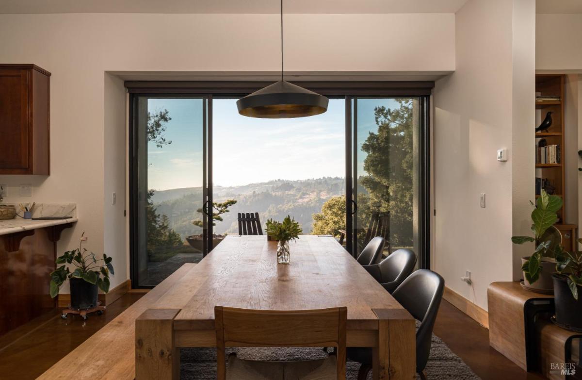 A table with chairs near sliding doors overlooking hills and trees.