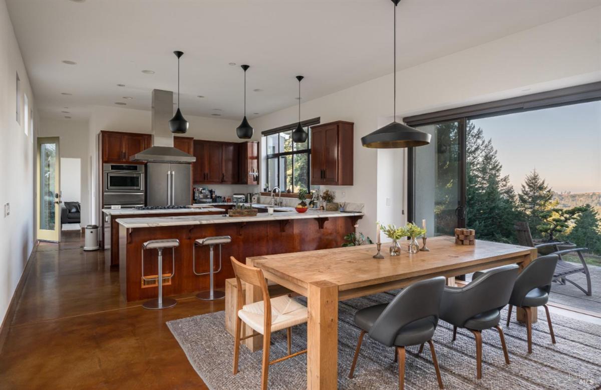 Dining area with table with chairs near sliding doors overlooking hills and trees.