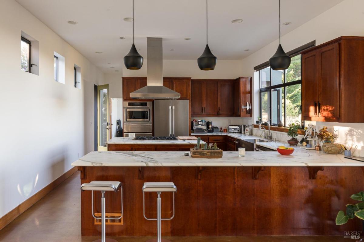 A modern kitchen with an island, wood cabinetry, and pendant lights.