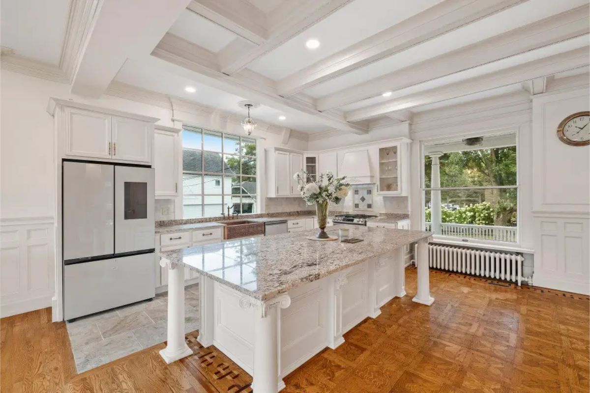 A large granite island with decorative columns, ideal for cooking and entertaining. Custom cabinetry, coffered ceilings, and large windows provide a bright and refined atmosphere.