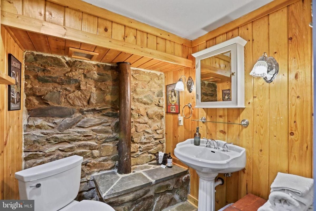 Rustic bathroom with stone walls, wooden trim, and pedestal sink.