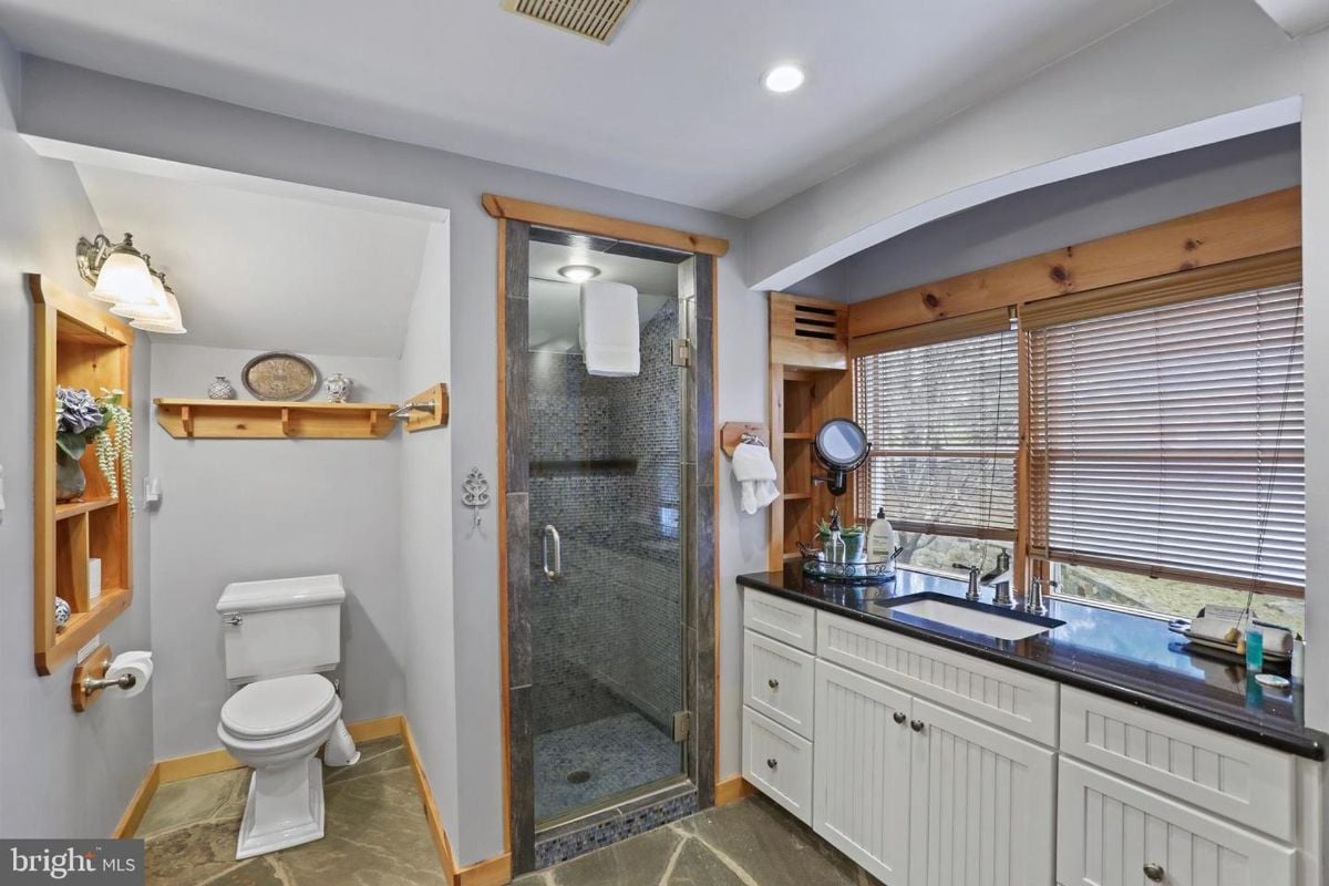 Sleek bathroom featuring a stone-tiled shower and expansive vanity with dark countertops.