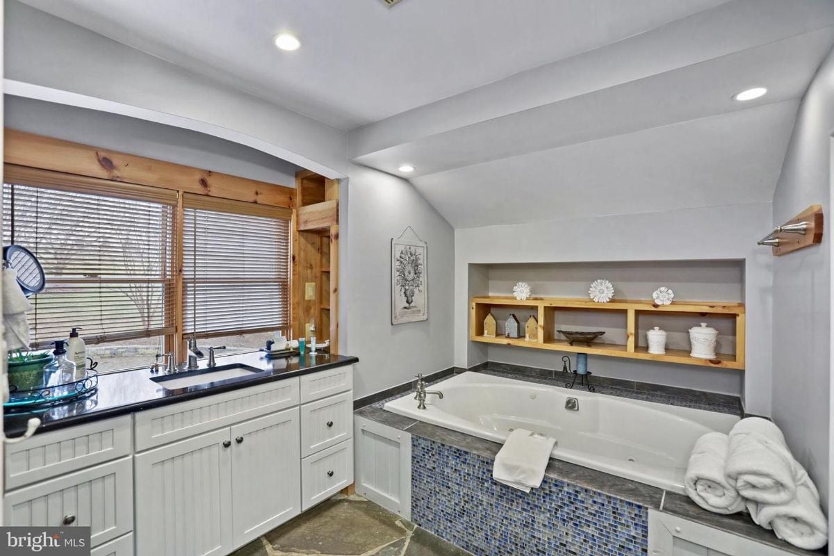 Spa-like bathtub setup with built-in shelving and a stone-tiled surround.