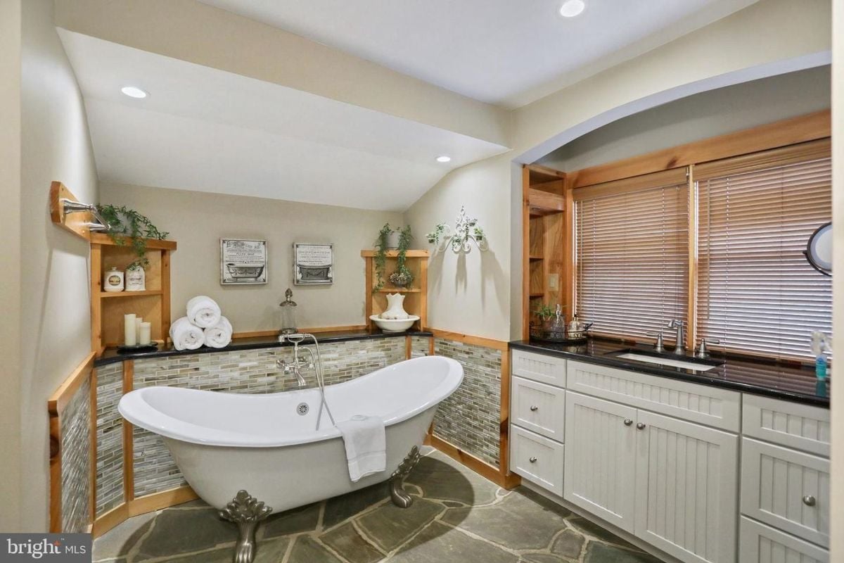 Clawfoot bathtub set against stone and wood-paneled walls in a cozy bathroom.