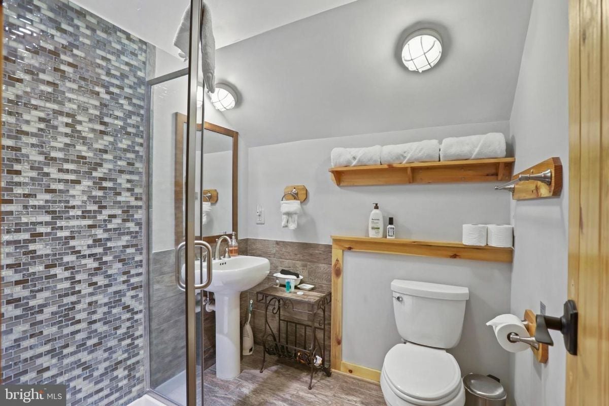 Compact bathroom featuring a tiled walk-in shower and minimalist wooden shelving.