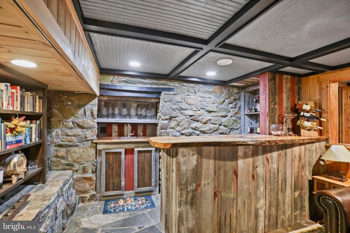 Rustic home bar with stone walls, reclaimed wood counter, and built-in shelves for wine storage.