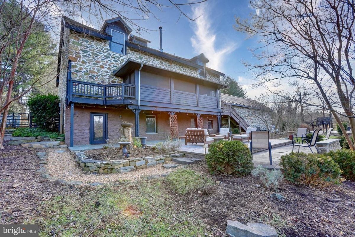 Rear exterior view showcasing a stone-walled home with a wraparound deck and patio area.
