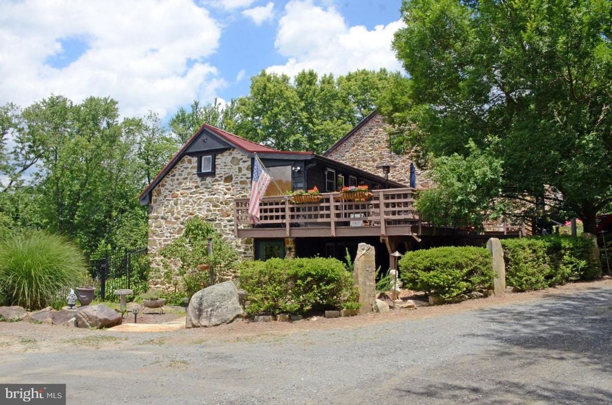 Stone-clad country home with an elevated wooden deck and mature trees lining the property.