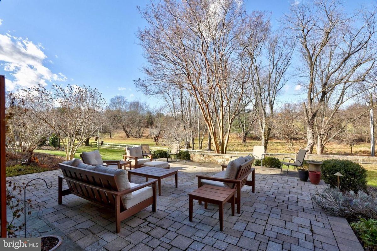 Open patio seating area with wooden furniture surrounded by lush landscaping and trees.