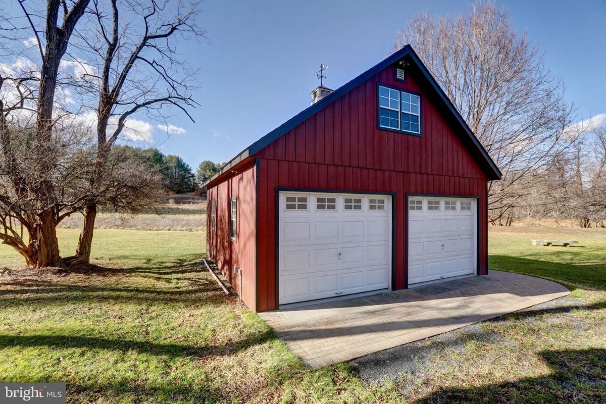 A red barn with two white garage doors sits on a grassy lawn.