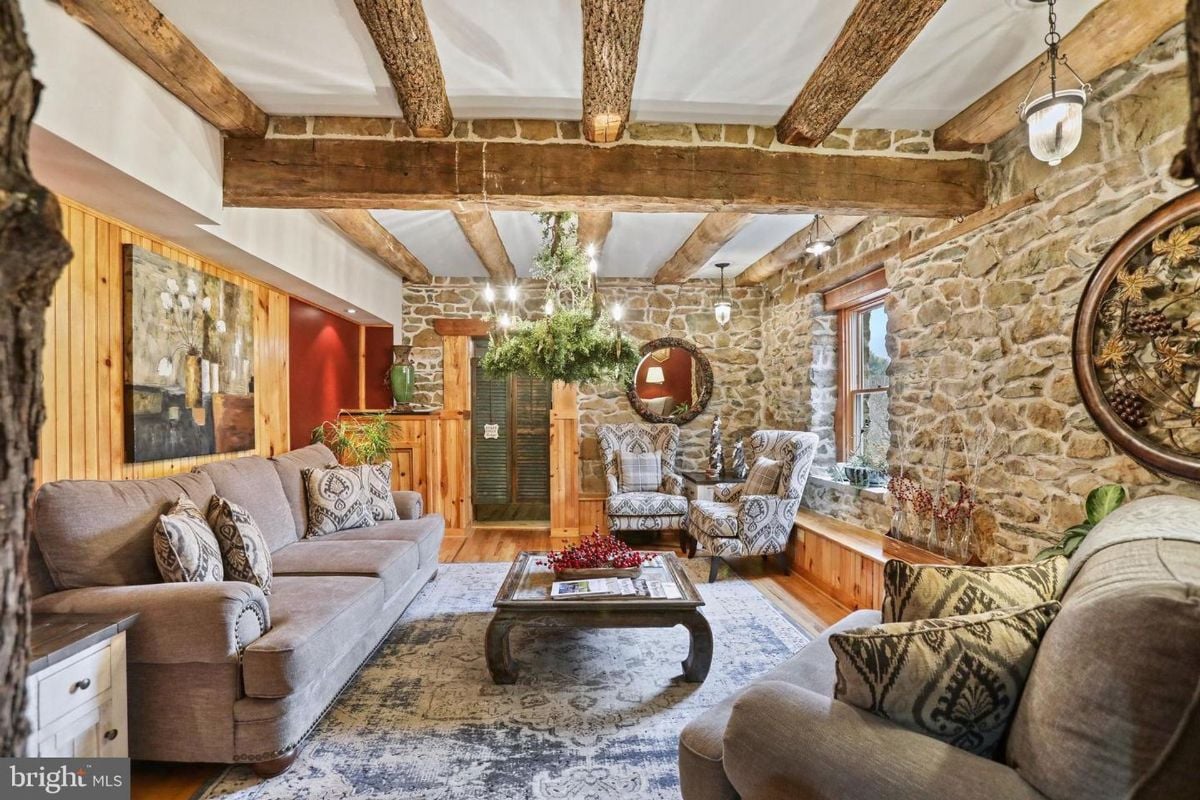 Cozy living room with exposed wooden beams, stone walls, and plush seating arrangements.