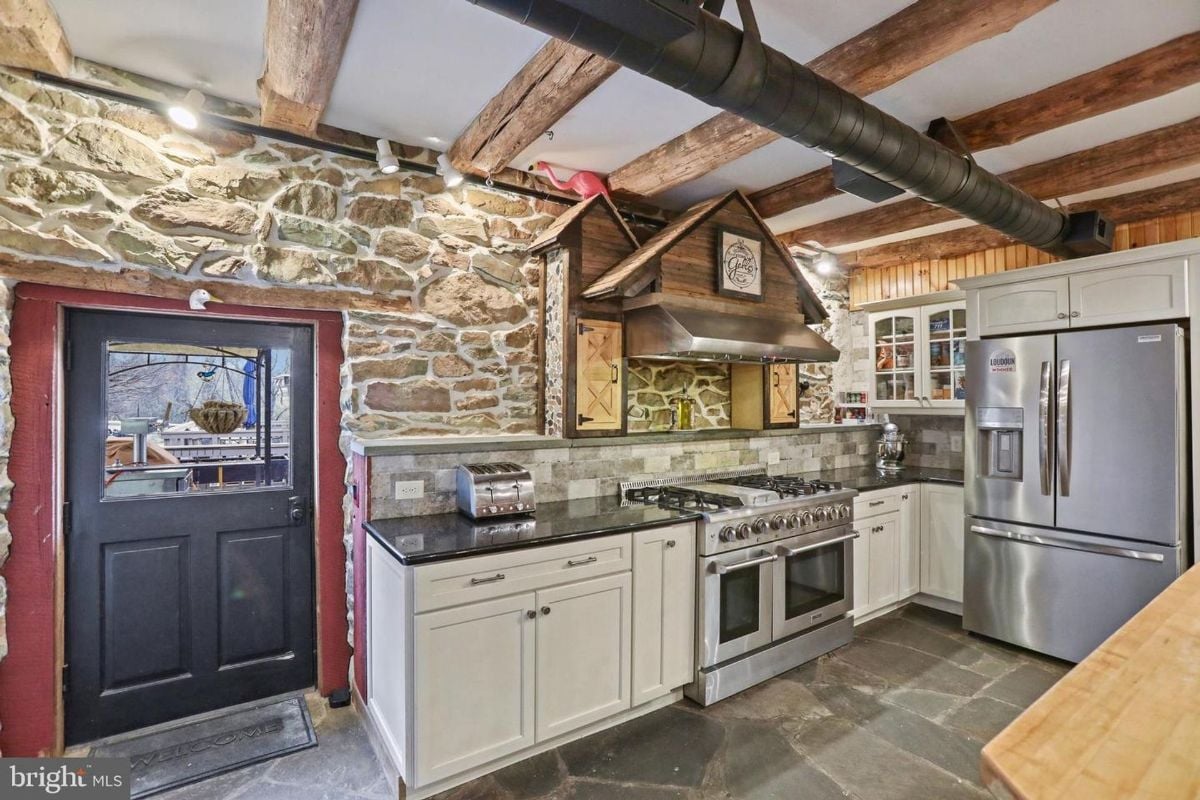 Chef’s kitchen featuring exposed beams, stone backsplash, and high-end stainless steel appliances.