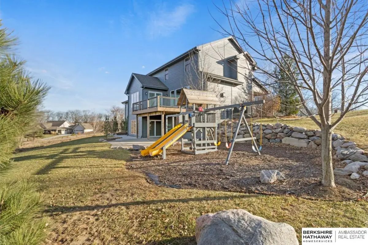 Expansive outdoor space featuring a children’s play structure with swings and a slide, surrounded by natural landscaping.