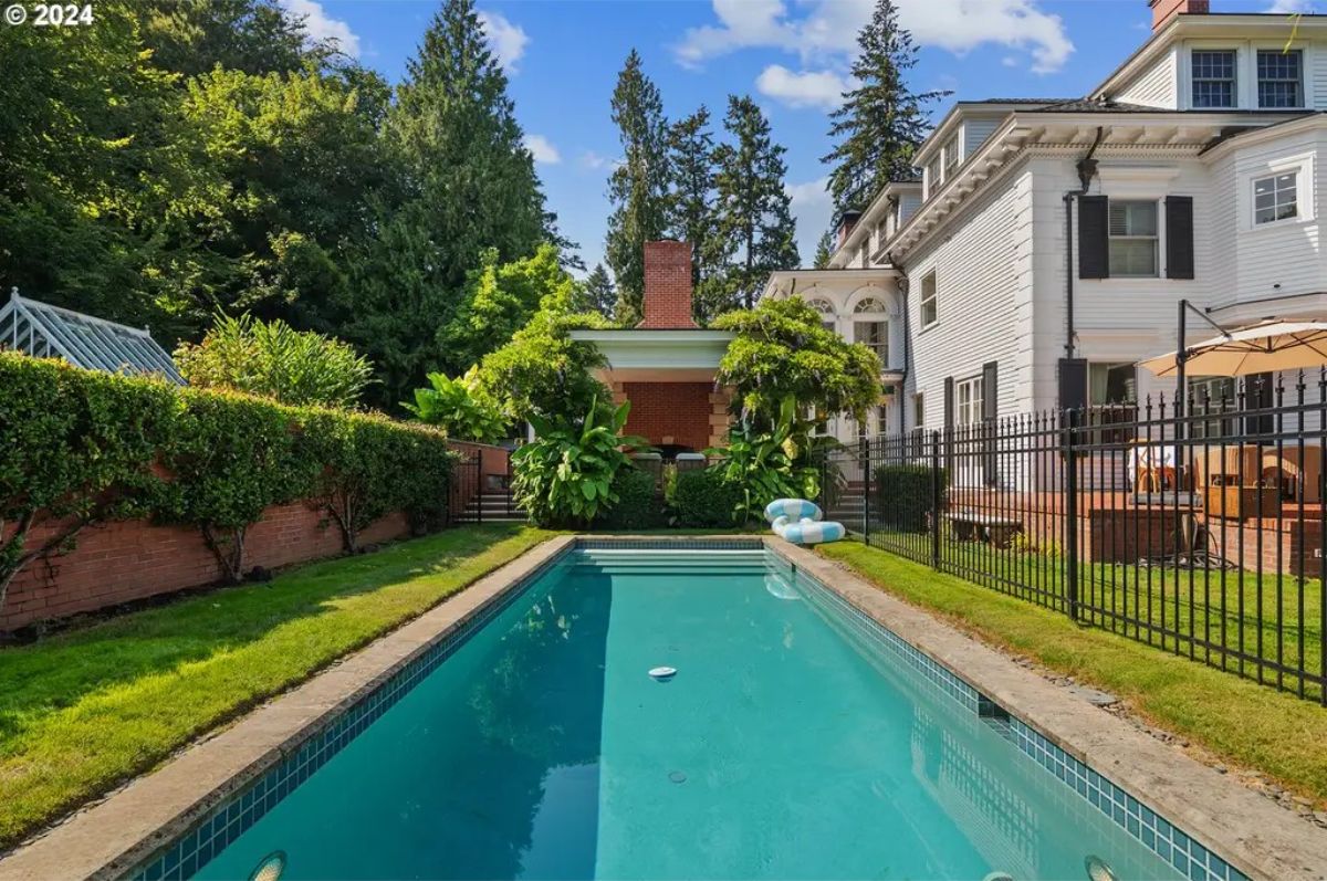 Rectangular pool is surrounded by manicured grass and brick walls lined with greenery.