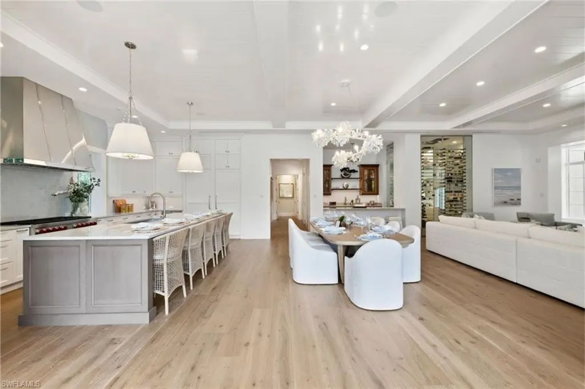 Large kitchen and dining area with white walls, wood flooring, and bright overhead lighting. 