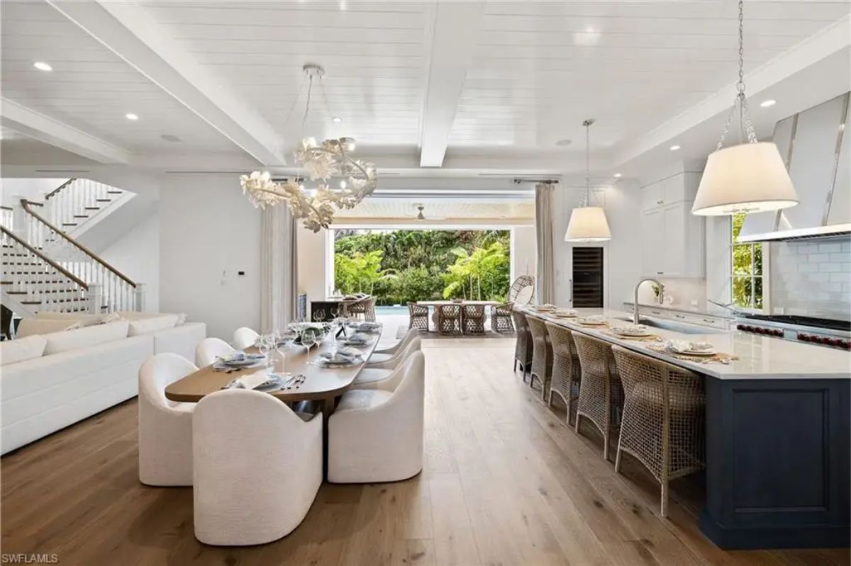 Open-concept dining and kitchen area featuring a long dining table with elegant chairs and a spacious kitchen island with barstools. 