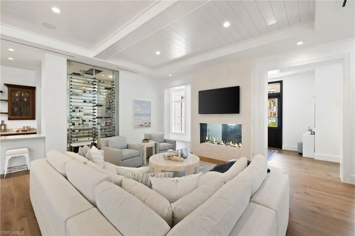 Living room with white furniture, a modern fireplace, and a wine storage unit behind glass doors. 