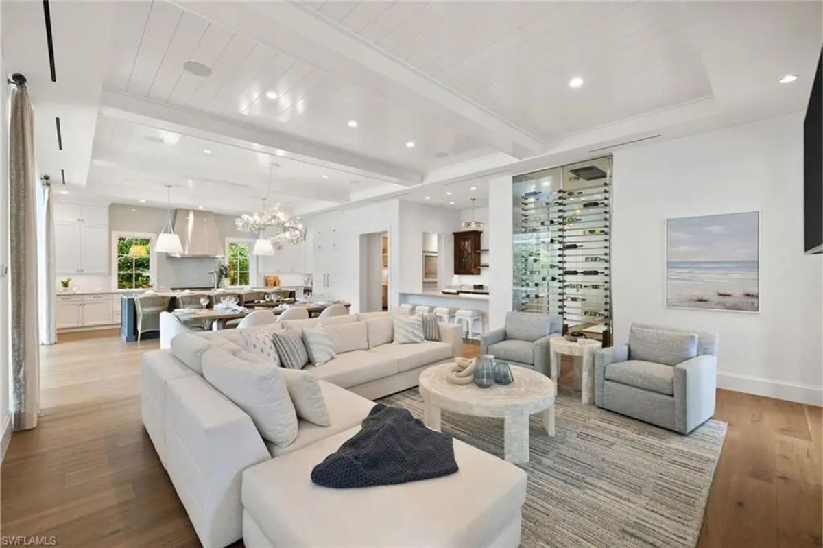 Living room with white furniture, a modern fireplace, and a wine storage unit behind glass doors. 