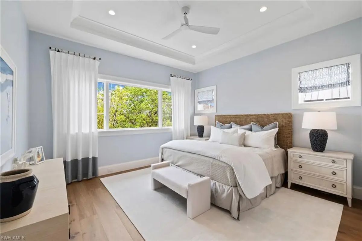 Bedroom with a natural wood bedframe, matching furniture, and bright windows offering an outdoor view. 
