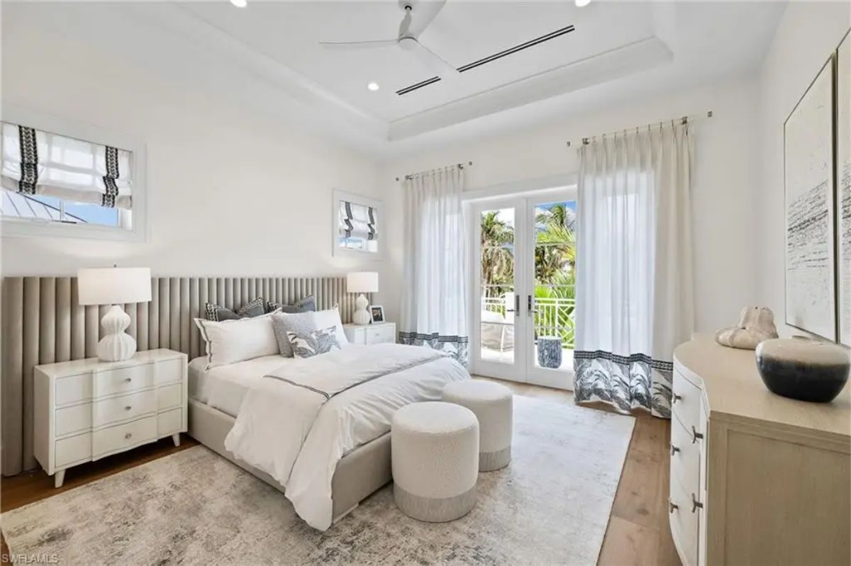 Bedroom with white and beige tones, featuring French doors leading to an outdoor space. 