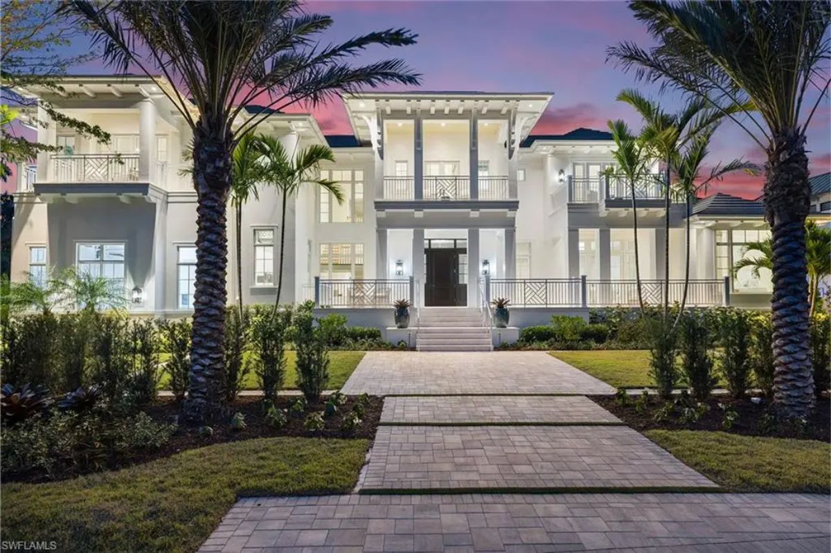 Exterior shot of a coastal-style home with large windows, palm trees, and a landscaped front yard. 