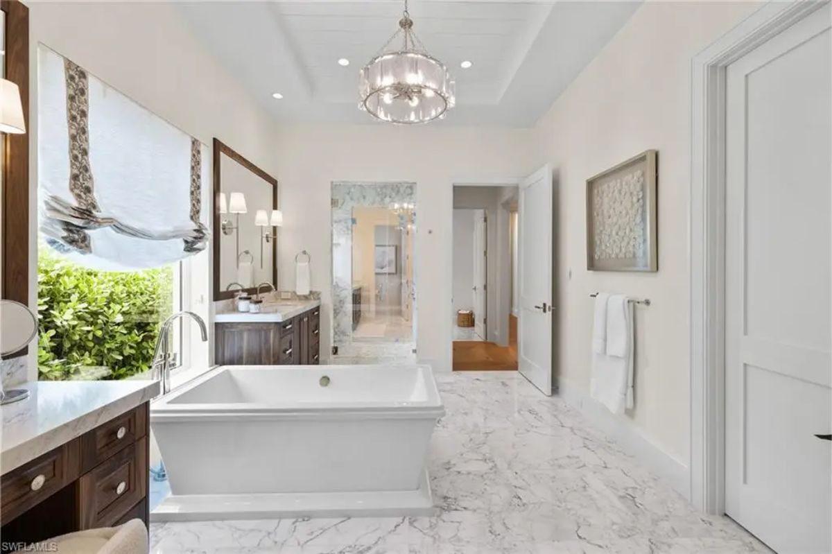Luxurious bathroom showcases marble flooring, freestanding tub, and expansive mirrors above double sinks. 