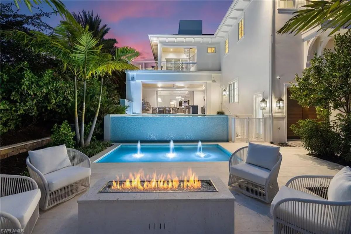 Backyard seating area with a fire pit, small pool fountains, and lush landscaping at dusk. 