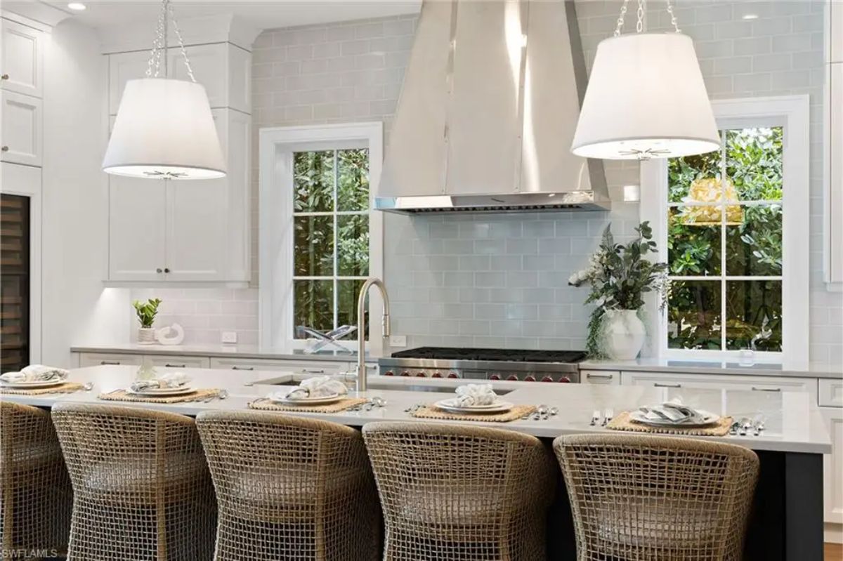 Kitchen space showcasing a modern stove with a stainless steel hood, white cabinetry, and wicker barstools along the island. 