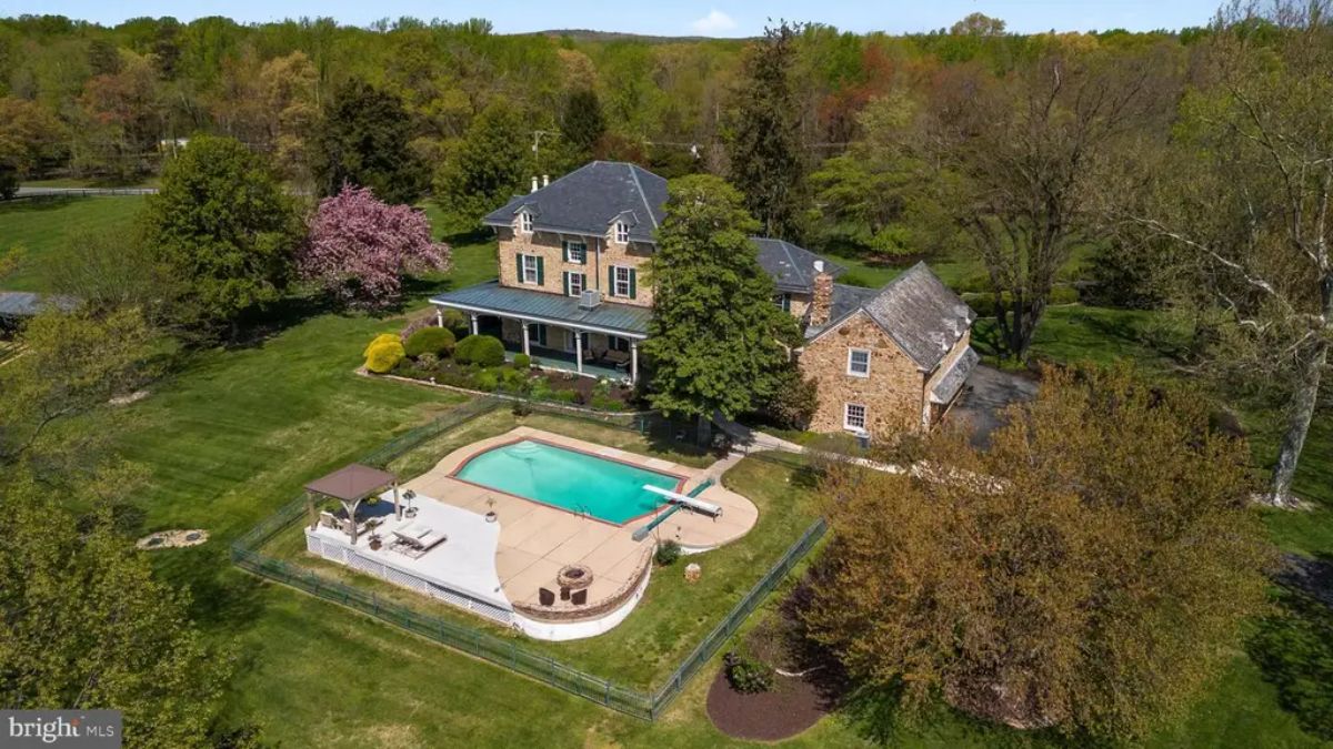 Stone house with a slate roof set amidst lush, manicured grounds and mature trees.