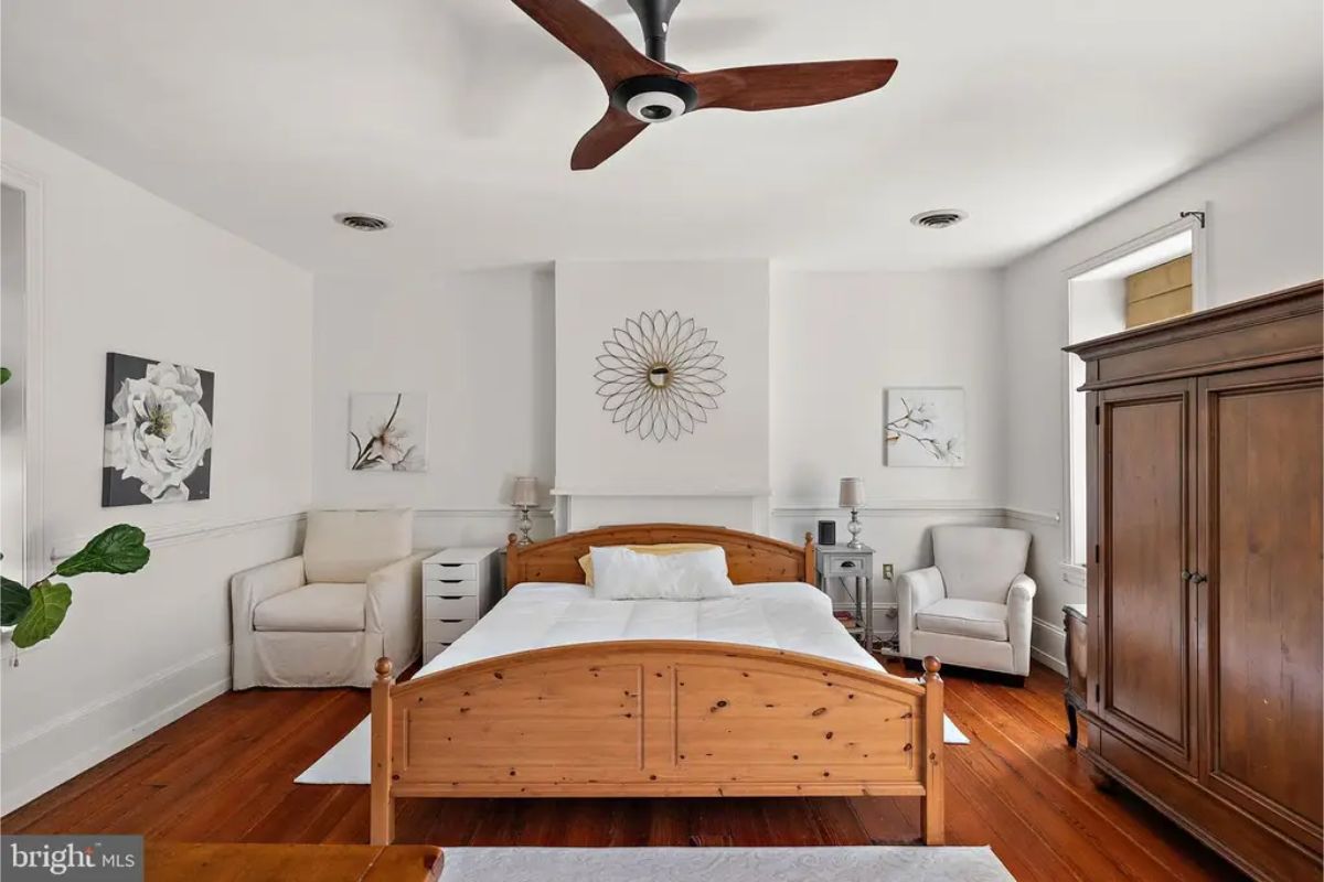 Room centers around a natural wood bedframe set against crisp white walls and wainscoting.