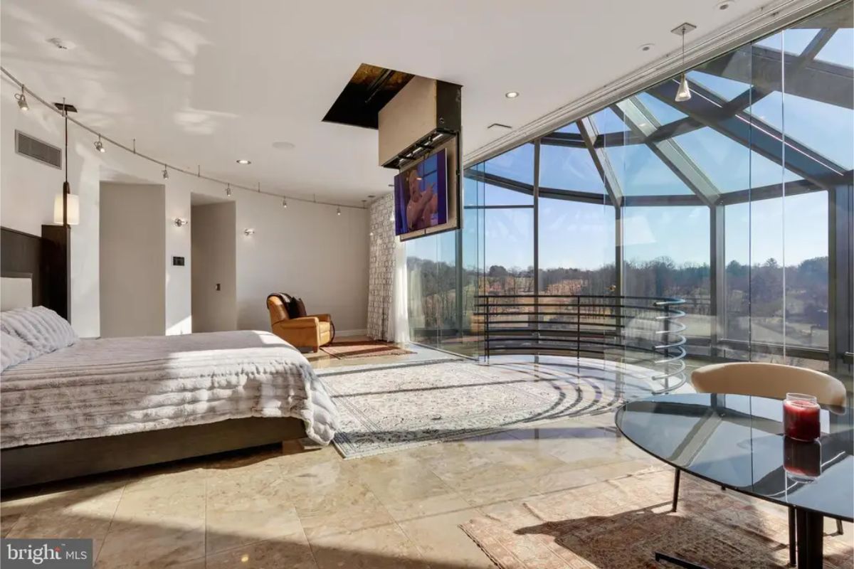 Master suite includes a seating area, glass walls, and a retractable ceiling-mounted TV. 
