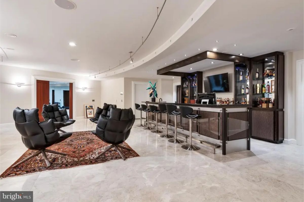 Home bar area offers a curved counter, leather seating, and a cozy lounge space with an elegant rug. 