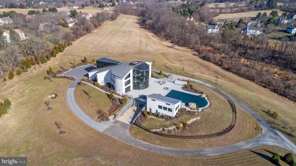 Wide aerial perspective emphasizes the property’s vast open surroundings and distinct curved driveway leading to the home. 