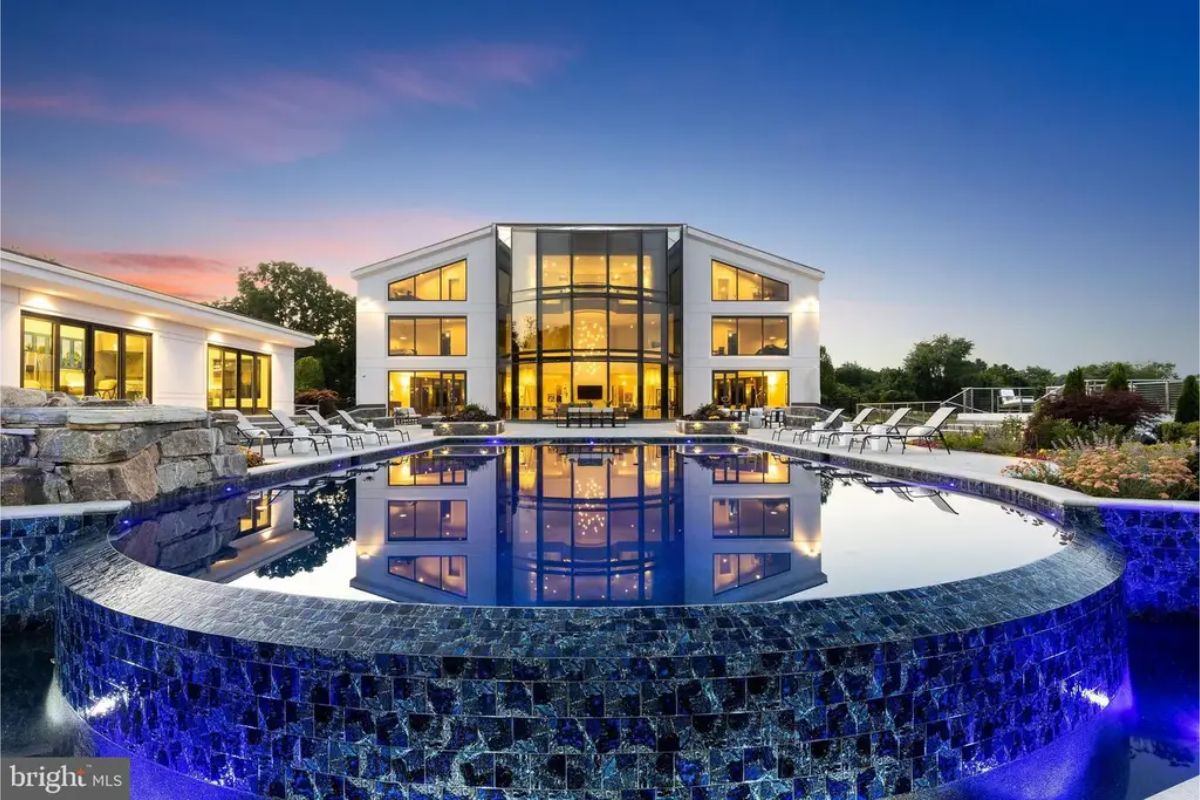 Rear exterior showcases a reflective infinity-edge pool with vibrant evening lighting against a modern glass facade. 