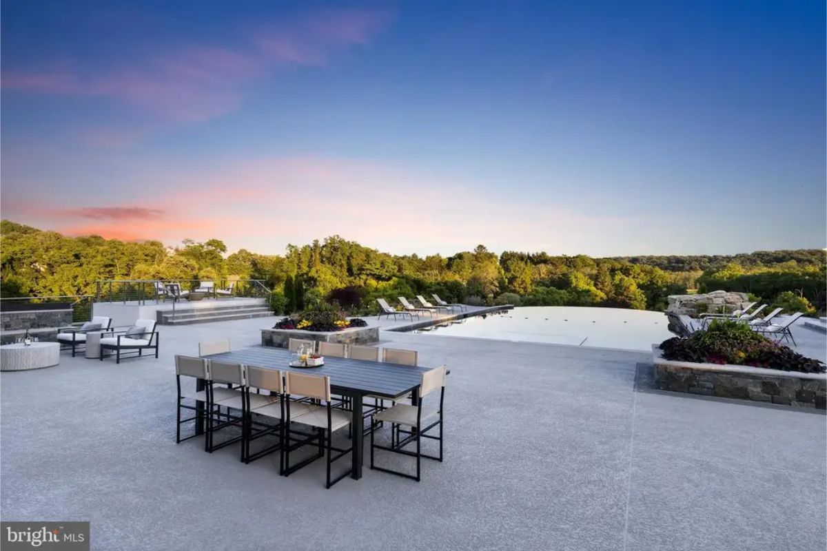 Outdoor area features an infinity pool, lounge chairs, and a dining table with a sunset view. 