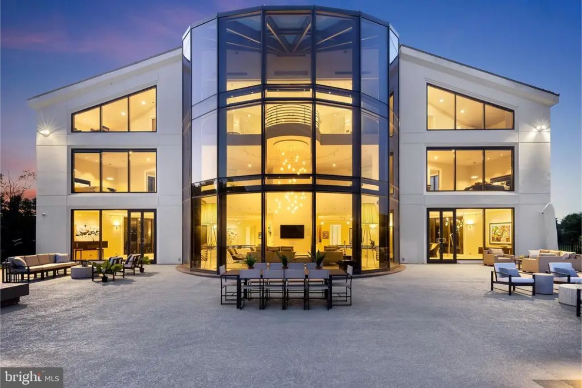 Frontal view of the house with grand curved glass architecture and lit interiors. 