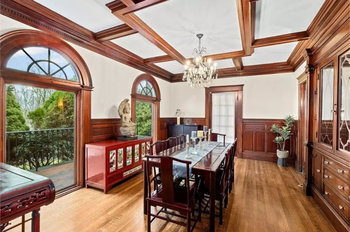 Exquisite craftsmanship with coffered ceilings, wainscoting, and arched wooden windows that frame lush outdoor views.