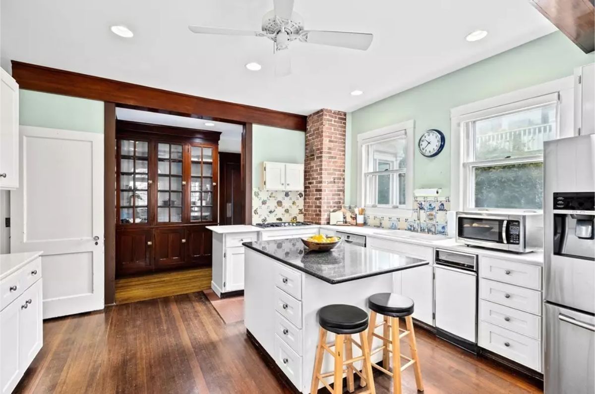 This airy kitchen combines modern functionality with rustic charm, featuring white cabinetry, a sleek black granite island, and warm hardwood floors.
