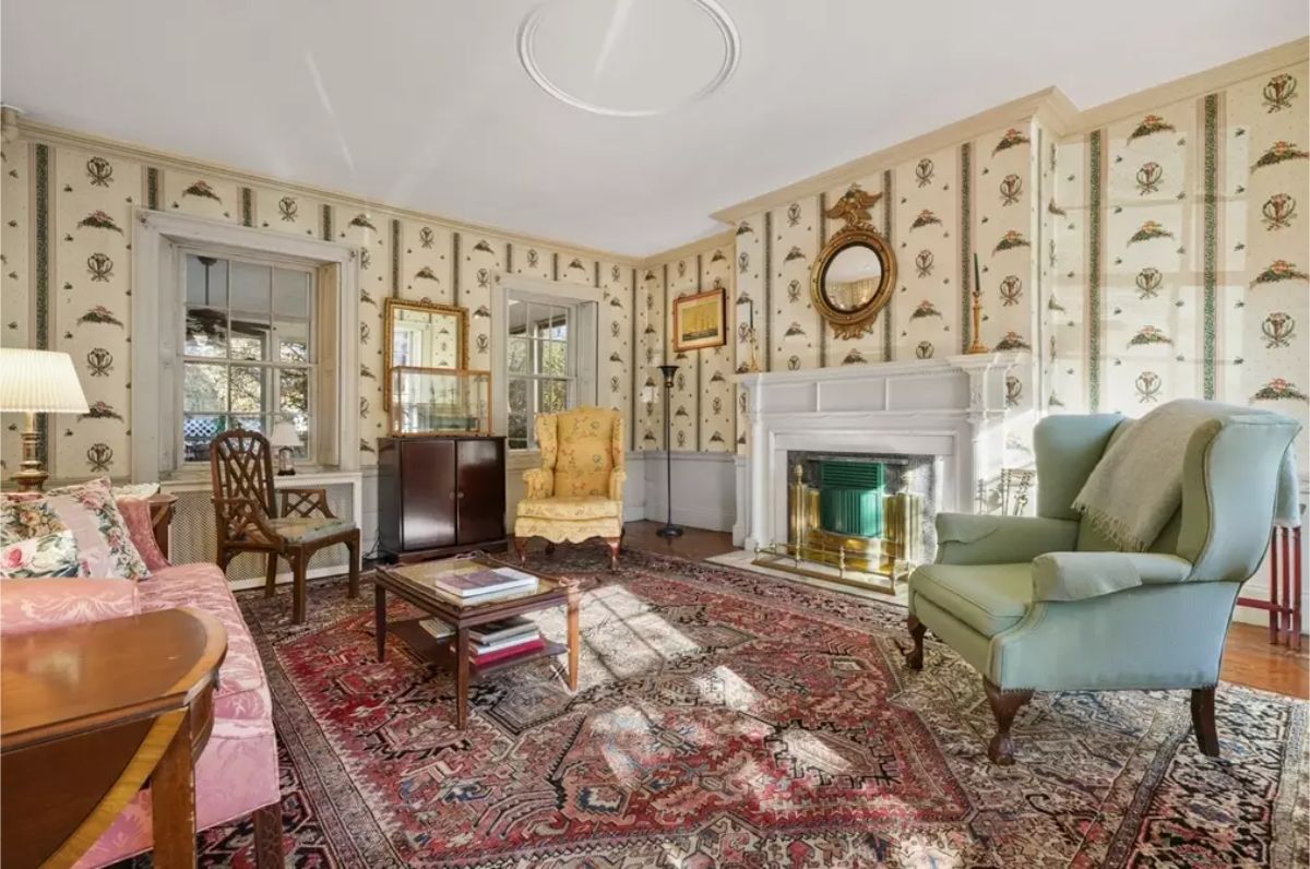 Cozy living room exudes a timeless appeal with its patterned wallpaper, antique-style furniture, and detailed area rug.