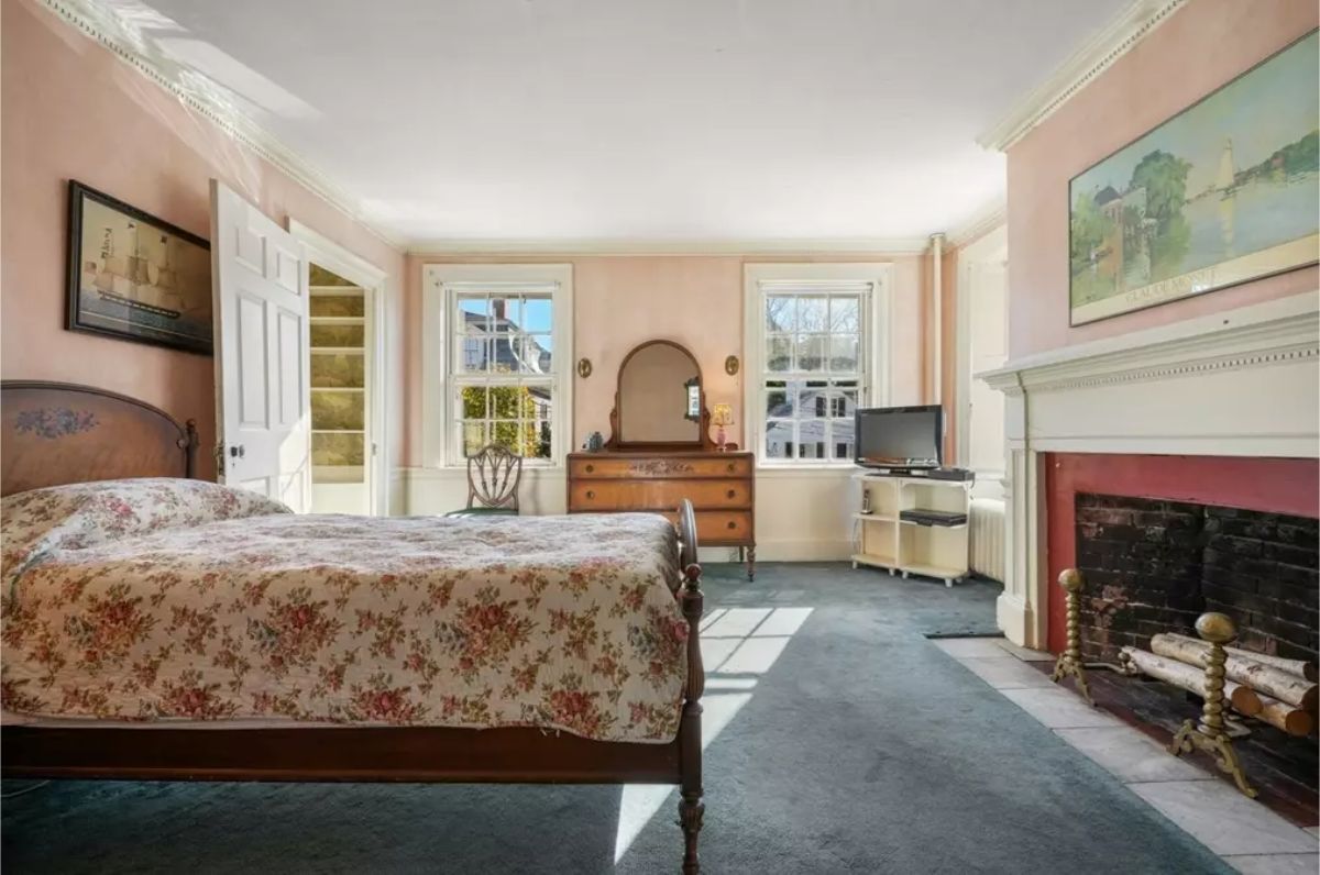 Bedroom combines vintage charm with natural light, featuring soft pink walls and traditional furnishings.
