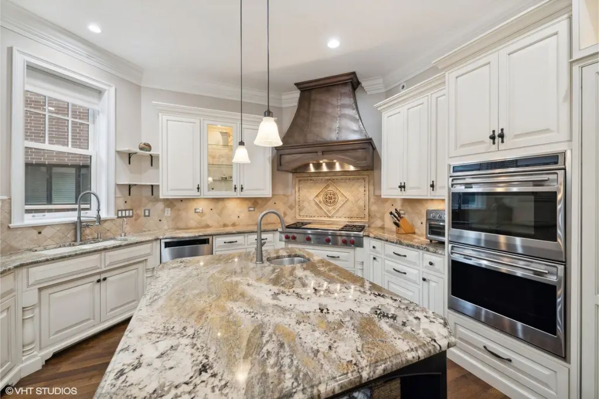 White cabinetry, a granite-topped island, and a copper range hood above the stove.